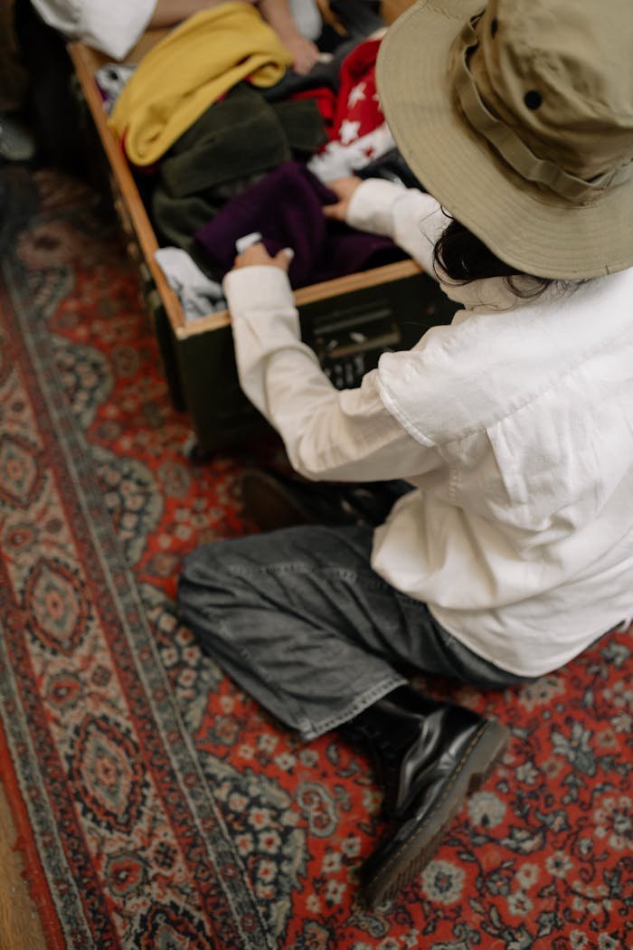 Personne en chapeau triant des vêtements dans une boîte en bois vintage sur un tapis à motifs à l