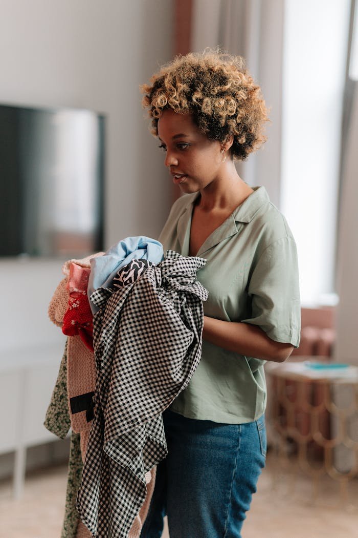 Focused woman sorting and holding a bundle of clothes at home, natural lighting.