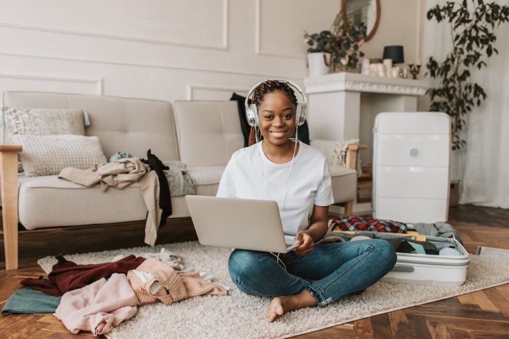 Jeune femme souriante entourée de bazar et utilisant un ordinateur portable dans un salon.